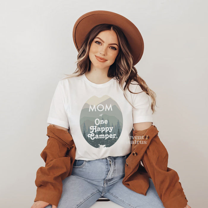 Smiling woman in a brown hat wearing a Mom of One Happy Camper shirt with green mountains.