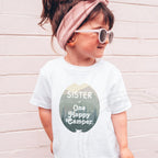 Girl in sunglasses and a pink headband wearing a white Sister of One Happy Camper shirt.
