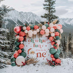 Vintage Santa first birthday backdrop topped with a balloon and pampas garland among snowy pines.