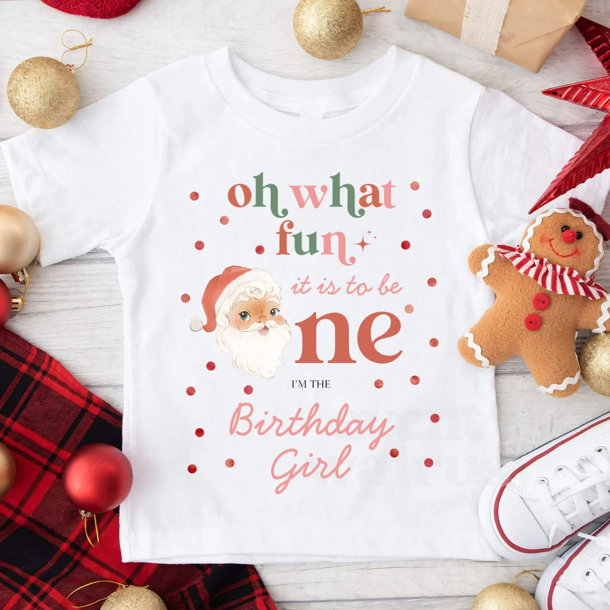 White Oh What Fun Birthday Girl tee laid flat with ornaments, a gingerbread man and red plaid.