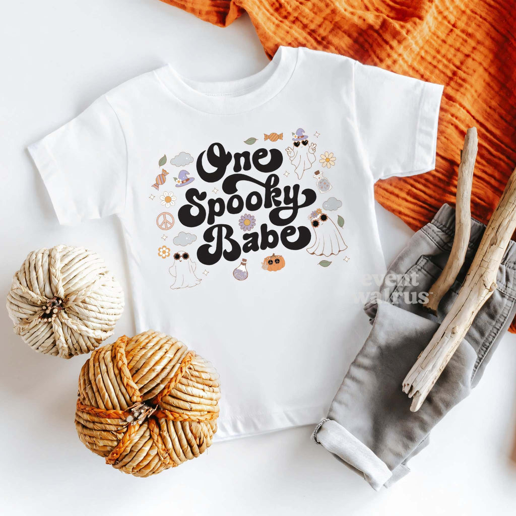 White One Spooky Babe baby tee laid flat with pumpkins and gray pants.