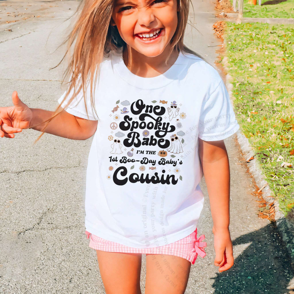 Laughing girl outdoors in a white One Spooky Babe Cousin kids tee.