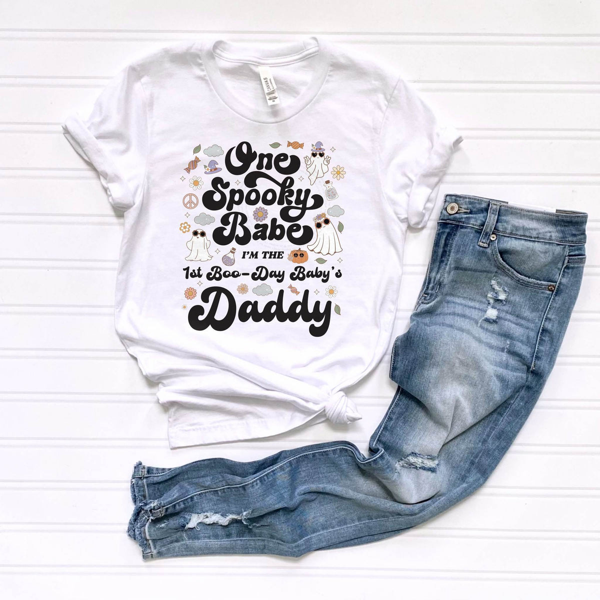 White One Spooky Babe Daddy tee laid flat beside jeans.