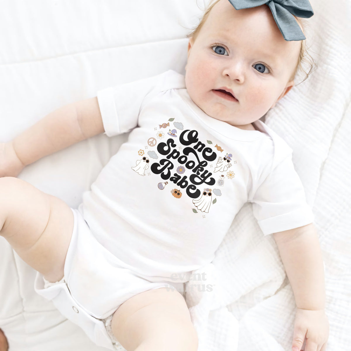 Baby girl with a gray bow lying in a white One Spooky Babe 1st Boo-Day bodysuit.