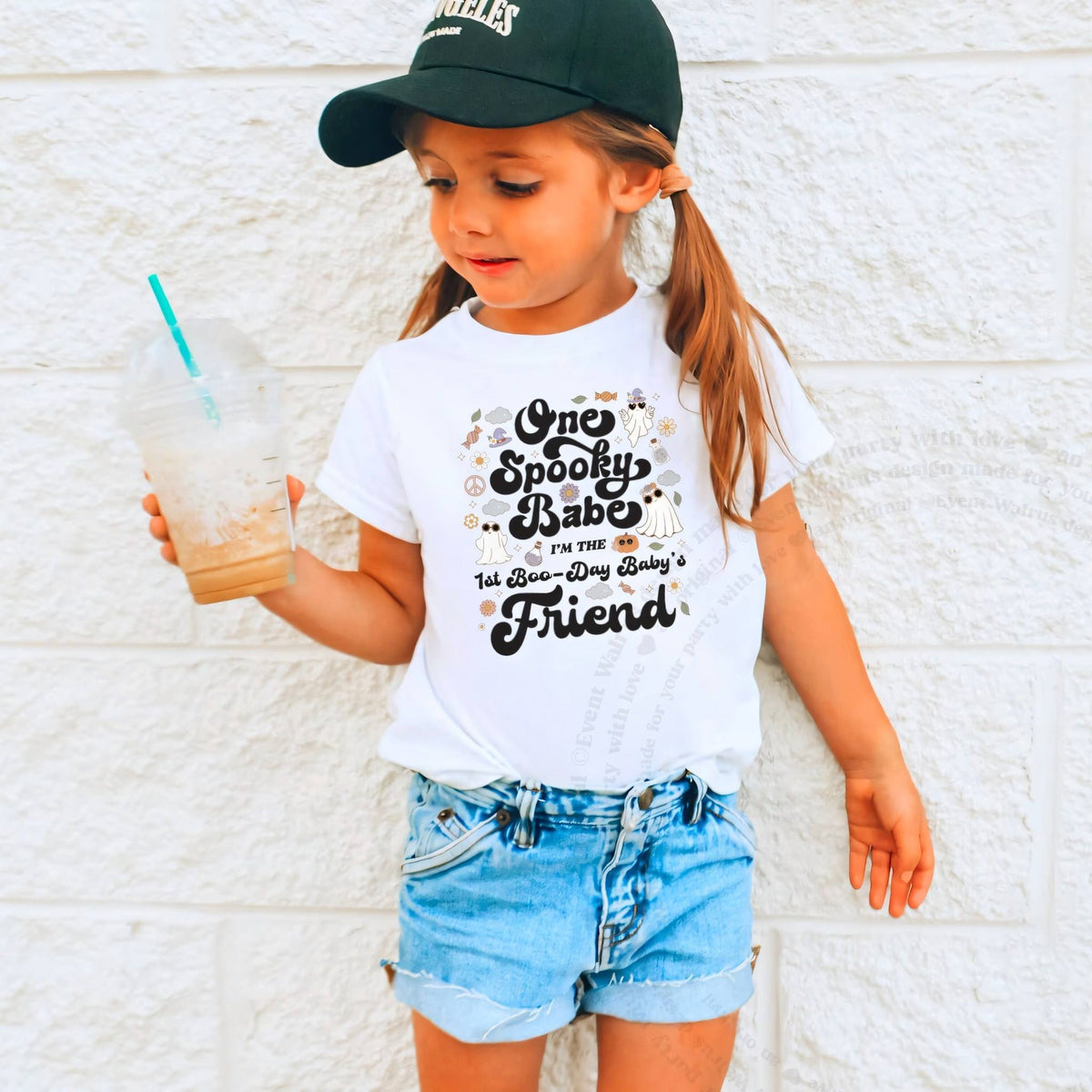 Girl in a ball cap holding a drink in a white One Spooky Babe Friend shirt.