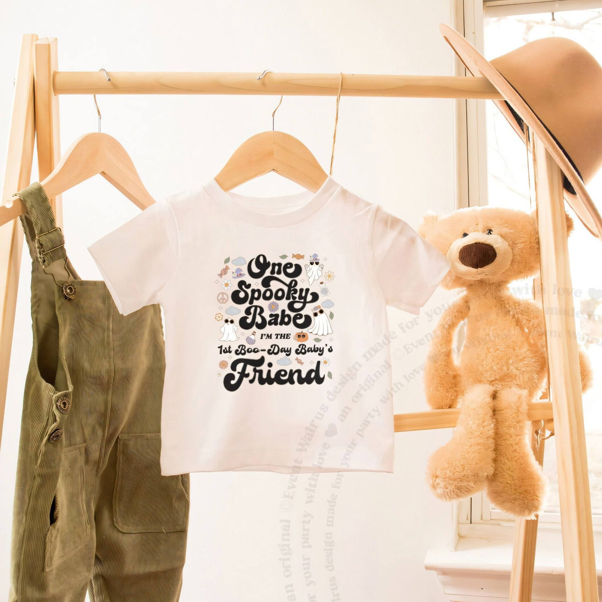 White One Spooky Babe Friend toddler tee on a wooden clothes rack beside a teddy bear.
