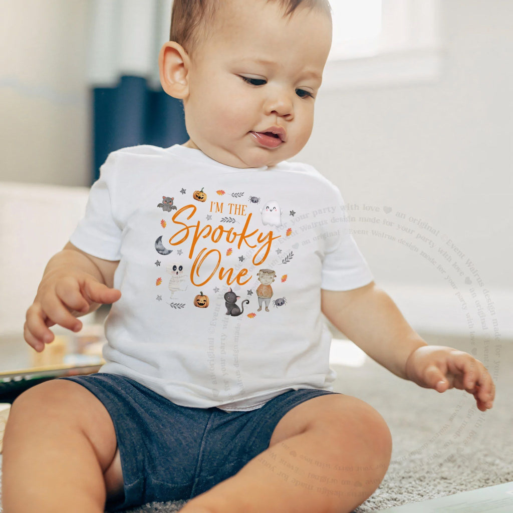 Baby boy sitting on a rug in a white I'm the Spooky One baby tee.