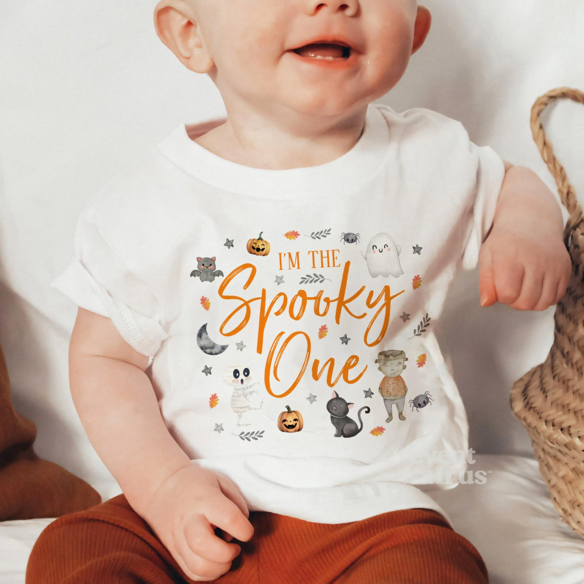 Baby sitting by a woven basket in a white I'm the Spooky One baby tee.