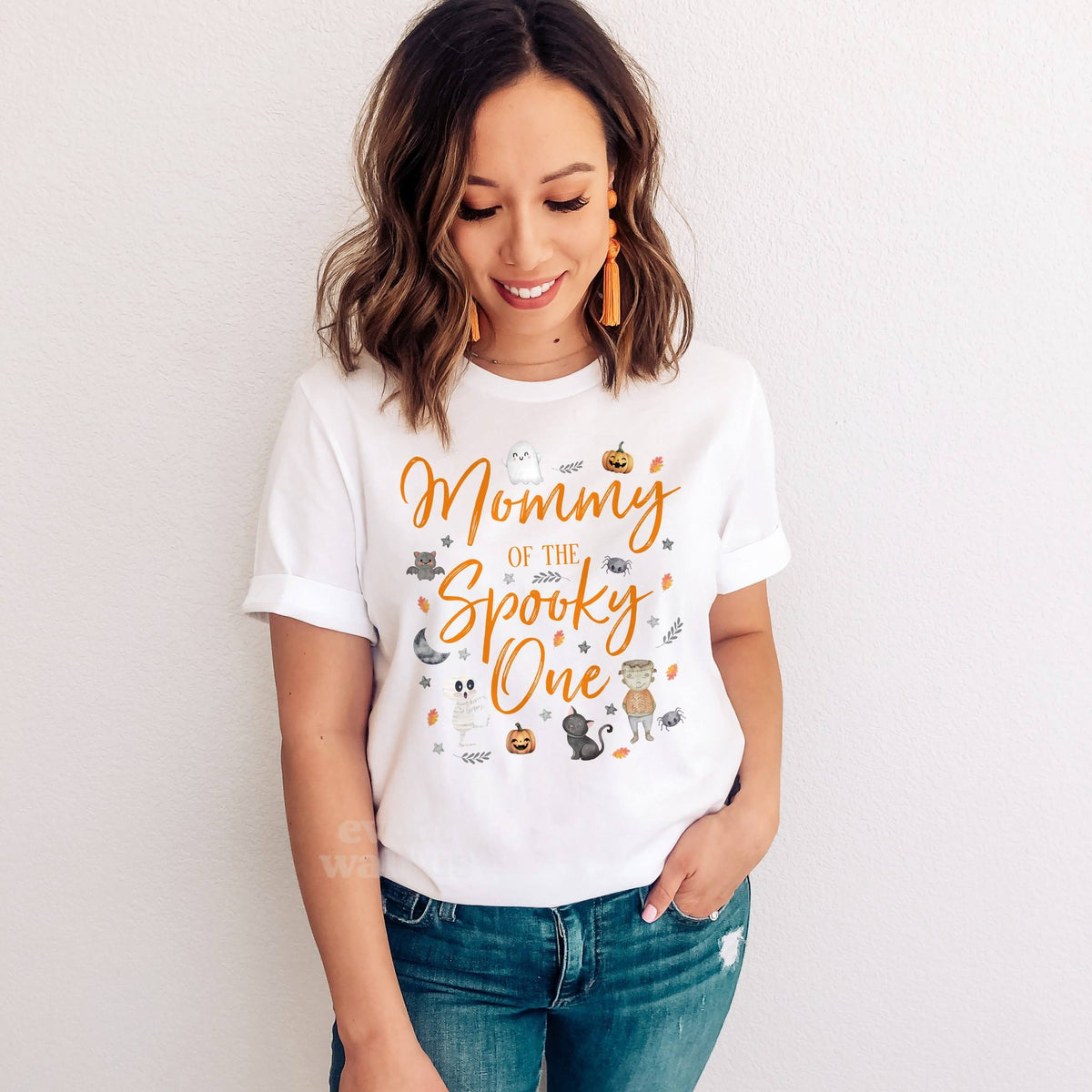 Smiling woman in jeans wearing a white Mommy of the Spooky One shirt.