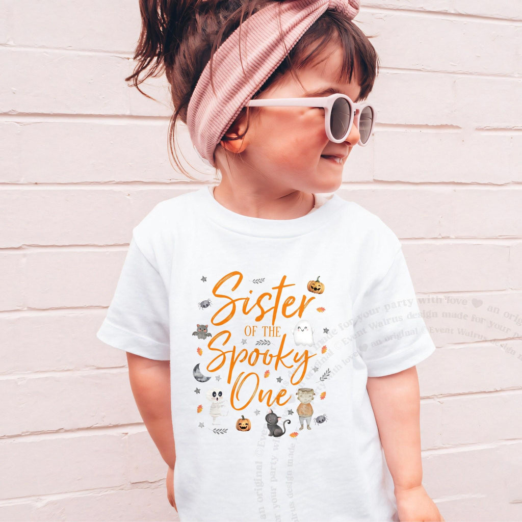 Girl in sunglasses and a pink headband wearing a white orange Sister of the Spooky One shirt.