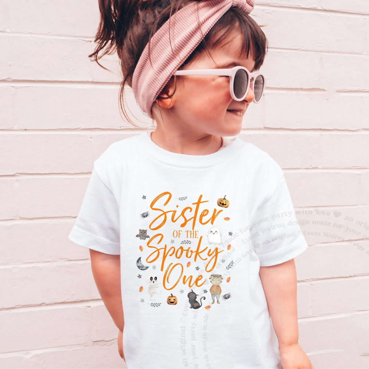Girl in sunglasses and a pink headband wearing a white orange Sister of the Spooky One shirt.
