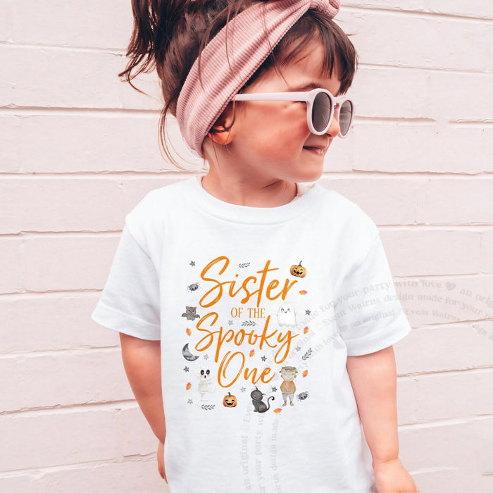 Girl in sunglasses and a pink headband wearing a white orange Sister of the Spooky One shirt.