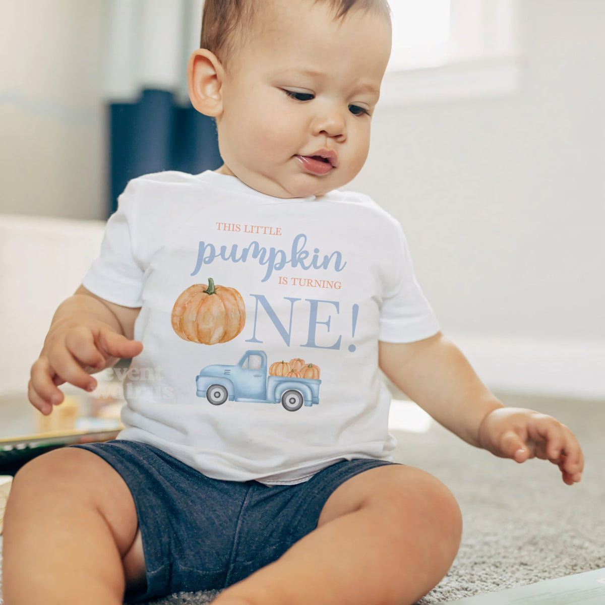 Baby boy sitting on a rug in a white Little Pumpkin baby tee.