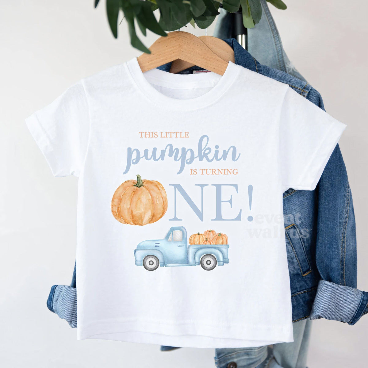 White This Little Pumpkin Is Turning One toddler tee on a hanger over a denim jacket.