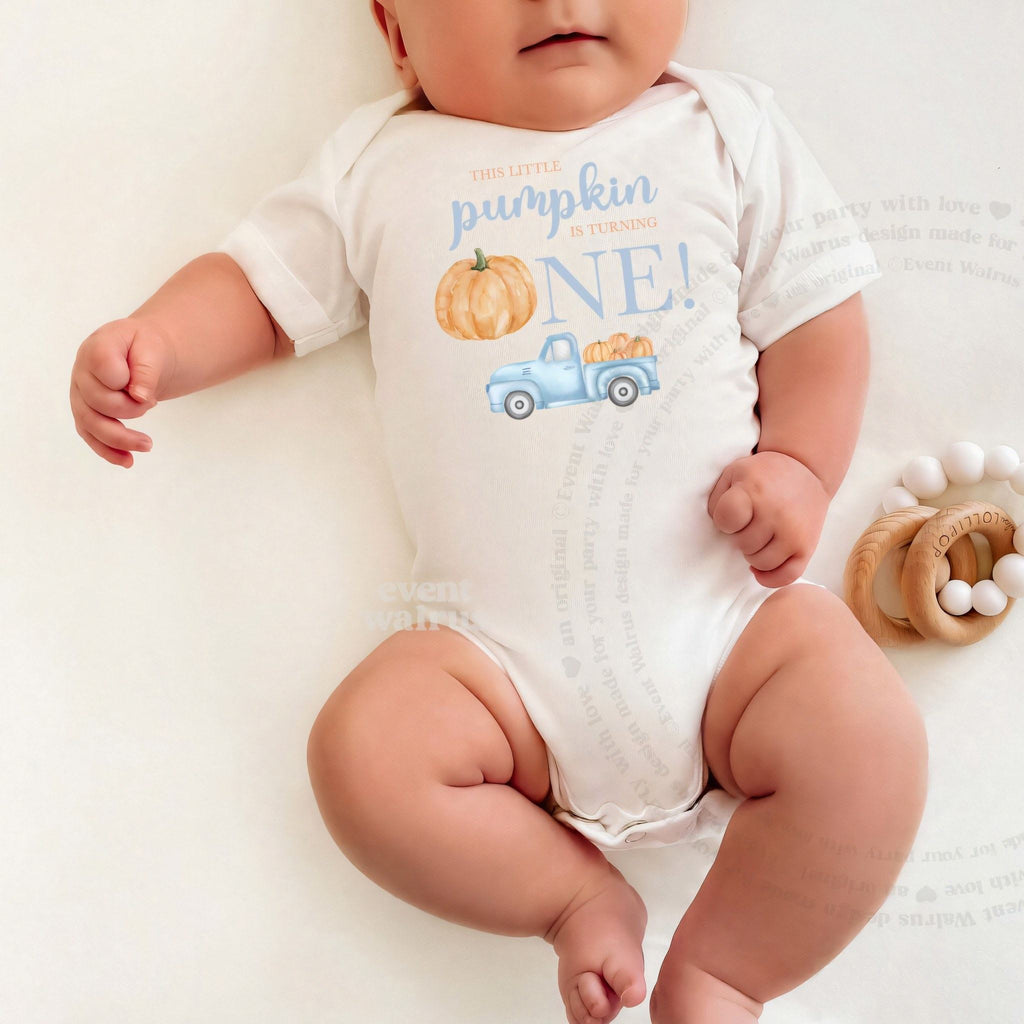 Baby lying on a white blanket in a white Little Pumpkin bodysuit with a blue truck.
