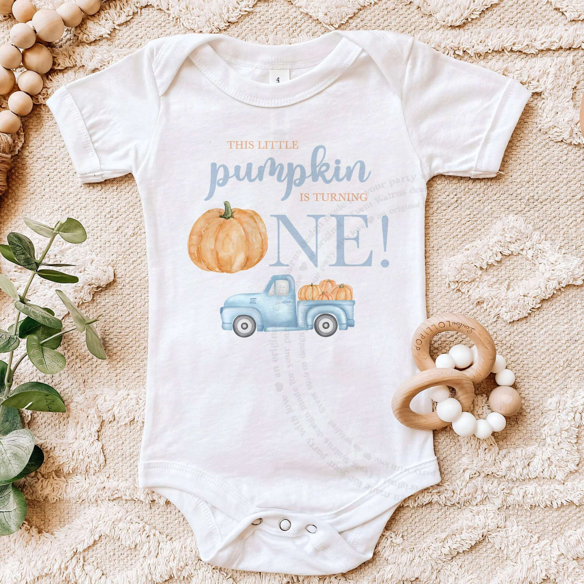 White Little Pumpkin bodysuit on a beige blanket with a wooden teether.