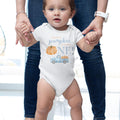 Baby taking steps while holding Mom's hands, in a white This Little Pumpkin Is Turning One bodysuit.