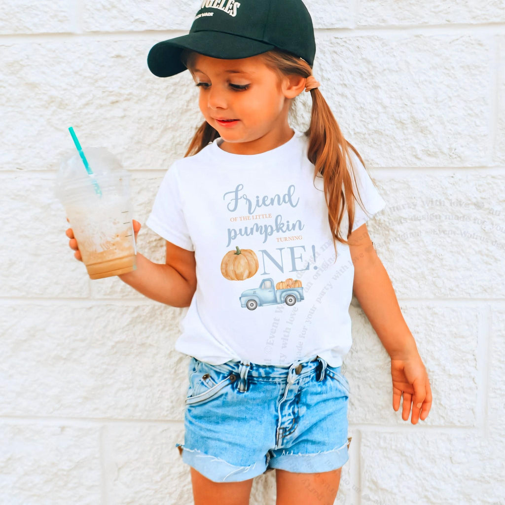 Girl in a ball cap holding a drink in a white Friend of the Little Pumpkin shirt.
