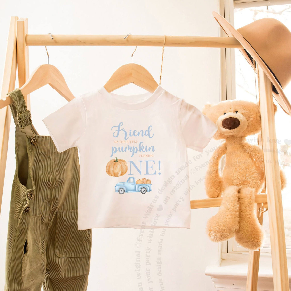 White Friend of the Little Pumpkin toddler tee on a wooden clothes rack beside a teddy bear.