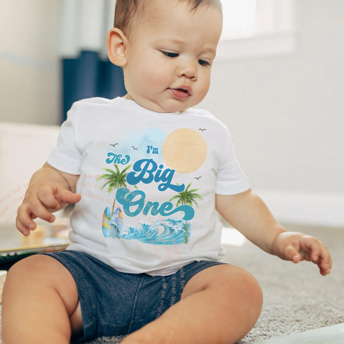Baby boy in a white I'm The Big One baby tee with a sun and a blue wave.