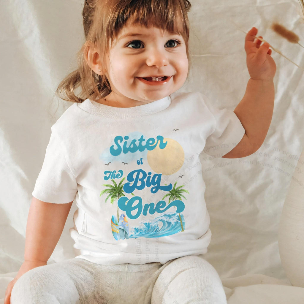 Smiling baby girl in a white Sister of The Big One baby tee.