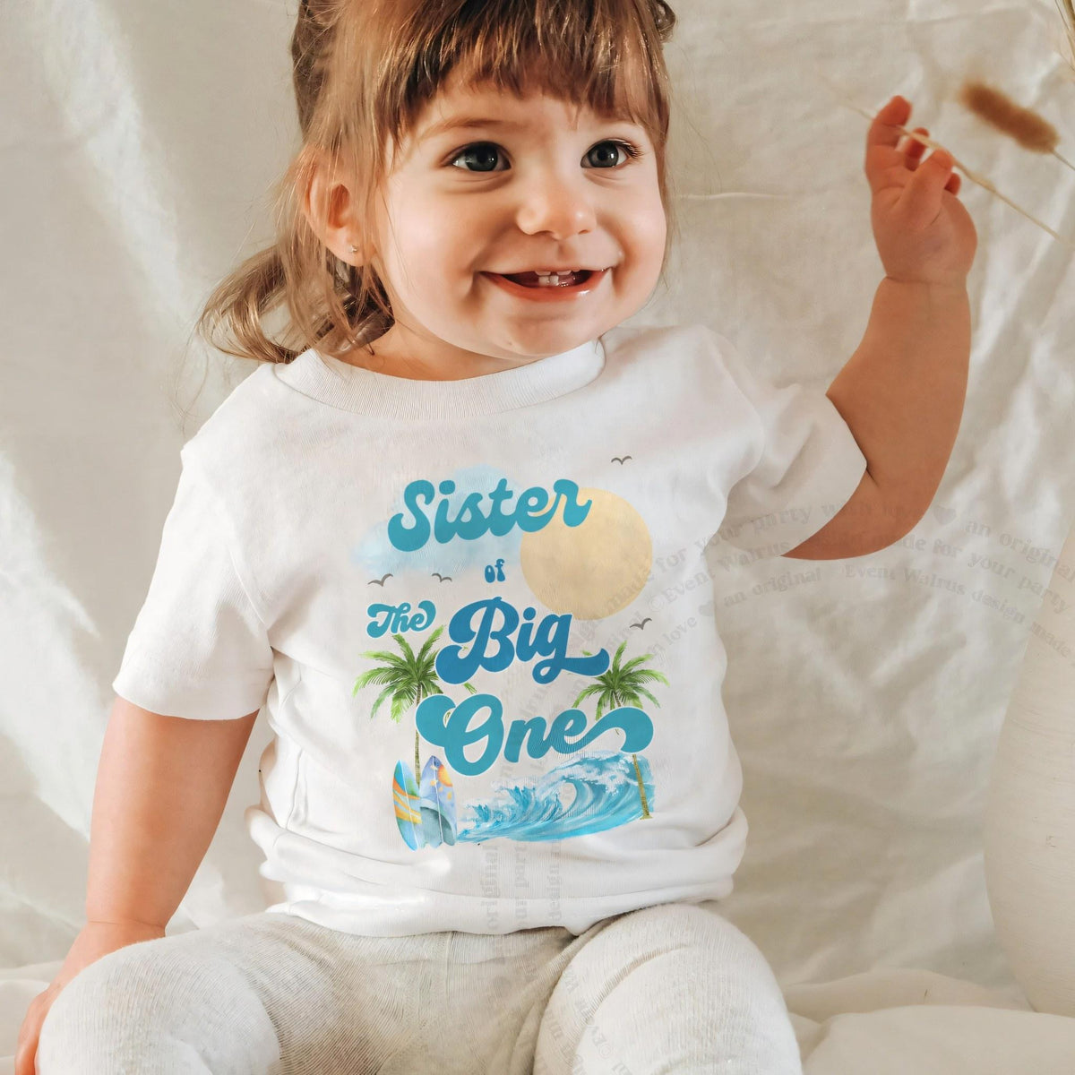 Smiling baby girl in a white Sister of The Big One baby tee.