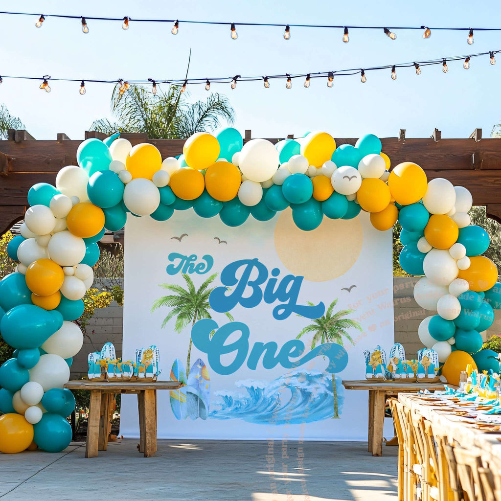 Palm Tree The Big One backdrop under a pergola with teal, white and yellow balloons.