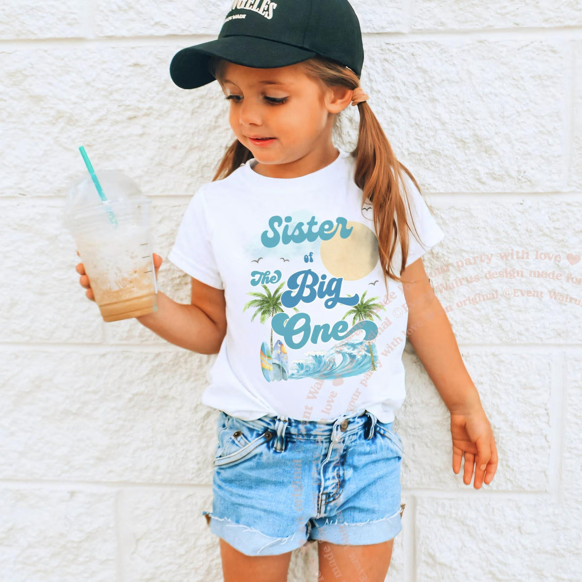 Girl in a ball cap wearing a white Sister of The Big One palm tree tee.