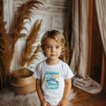 Little boy in a white Brother of The Big One palm tree shirt.