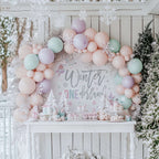 Winter onederland girl backdrop behind a white dessert table with frosted mini trees and pastel balloons.