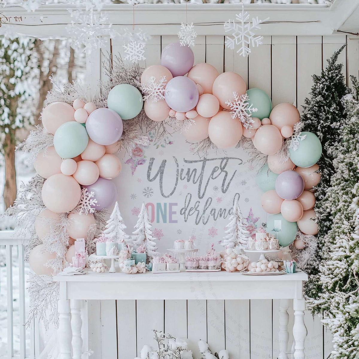 Winter onederland girl backdrop behind a white dessert table with frosted mini trees and pastel balloons.