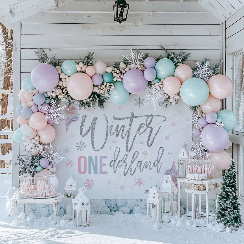 Pastel rose winter onederland backdrop on a snowy porch under a balloon and greenery garland.