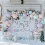 Pastel rose winter onederland backdrop on a snowy porch under a balloon and greenery garland.