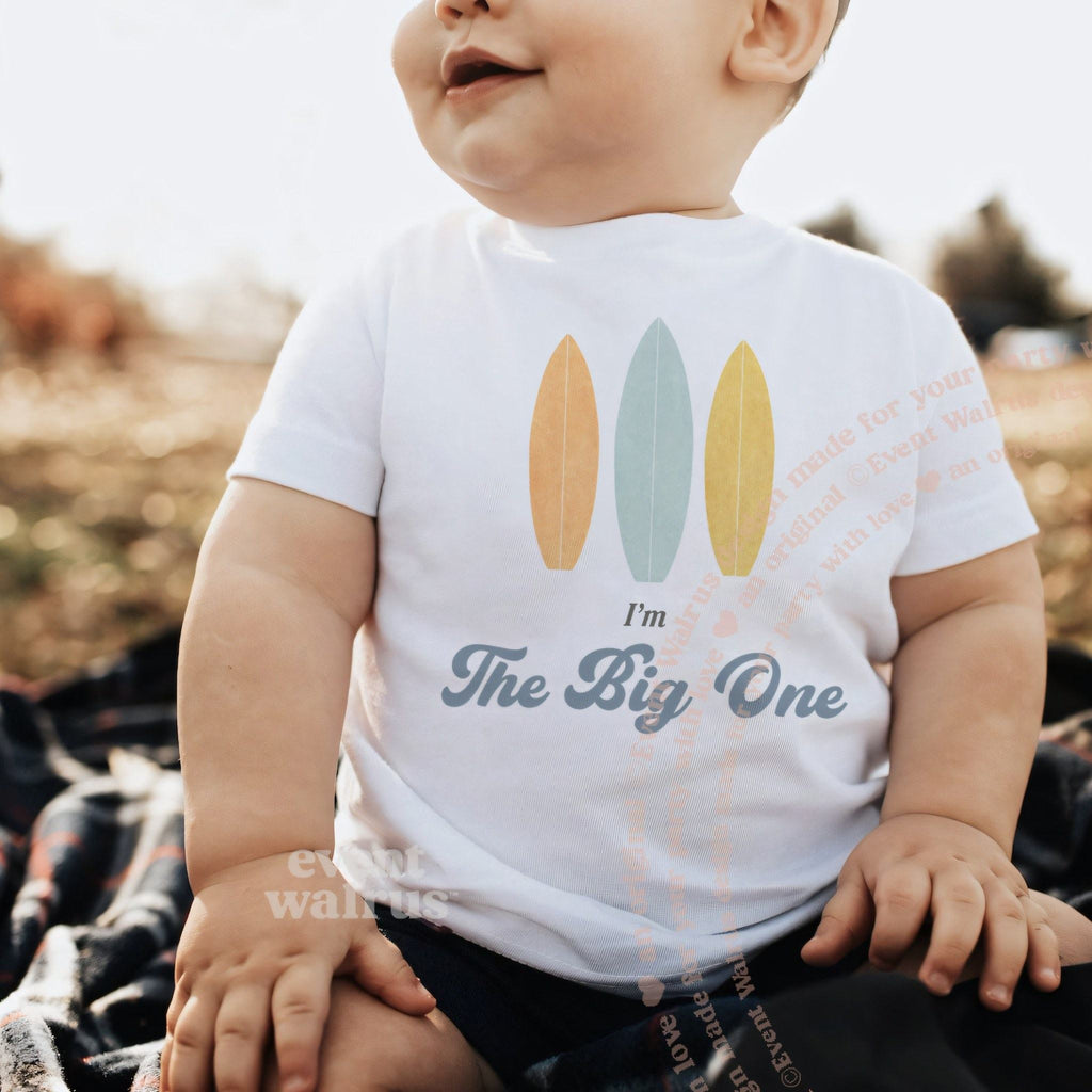 Baby sitting outdoors in a white I'm The Big One surfboard baby tee.