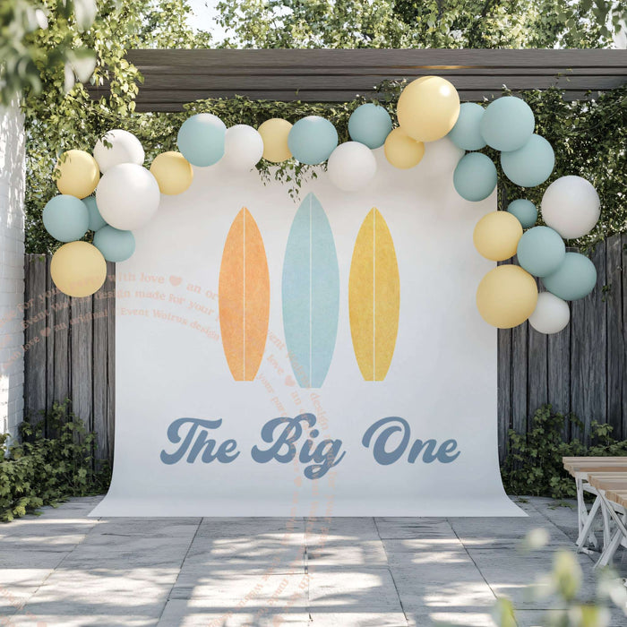 Pastel Surfboard The Big One backdrop on a patio under a blue, yellow and white balloon garland.
