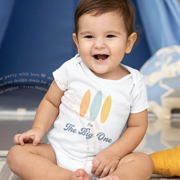 Smiling baby in a white I'm The Big One bodysuit with three pastel surfboards.