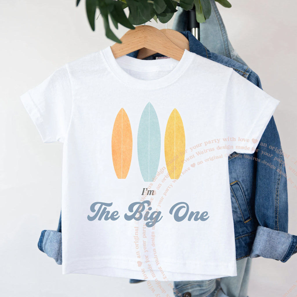 White I'm The Big One toddler shirt with pastel surfboards on a wooden hanger.