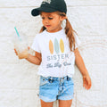Girl in a ball cap wearing a white Sister of The Big One surfboard tee.