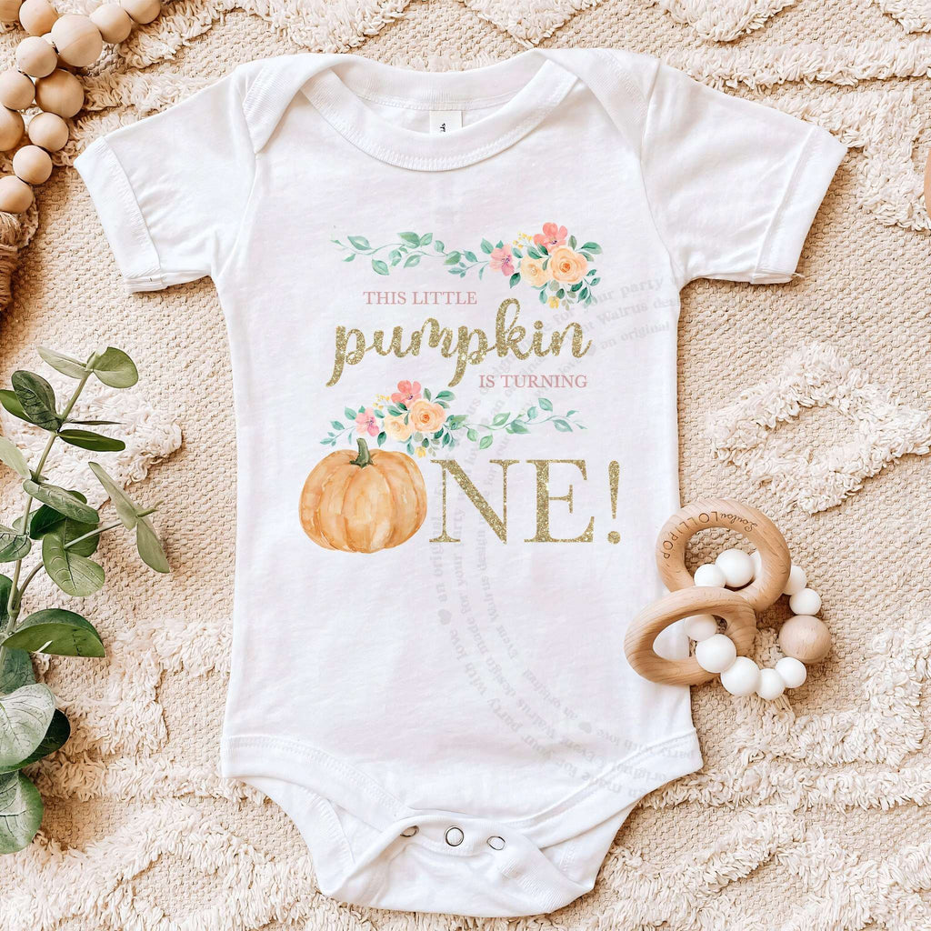 White floral Little Pumpkin bodysuit on a beige blanket with a wooden teether.