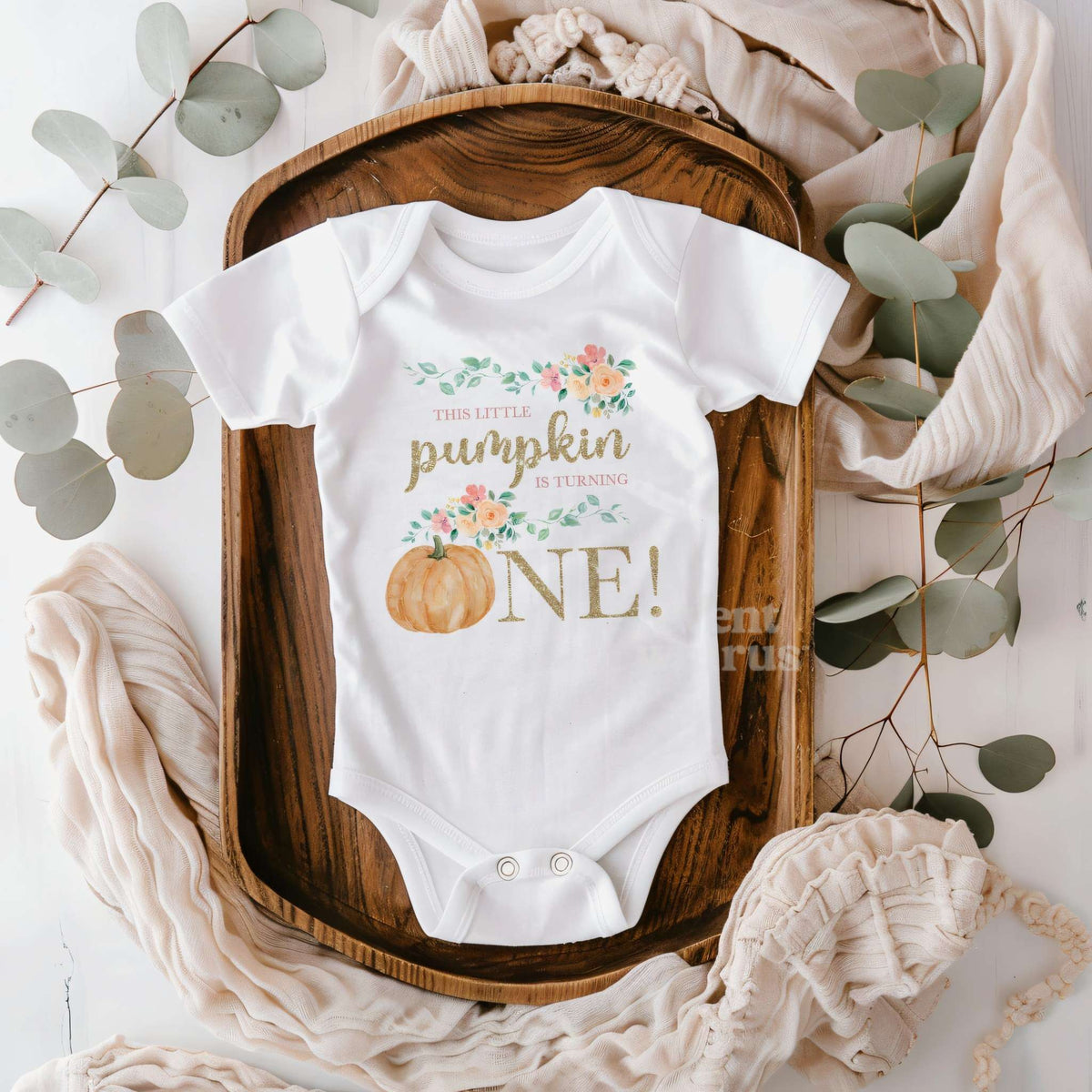 White Little Pumpkin bodysuit on a wooden tray with eucalyptus and a knit blanket.