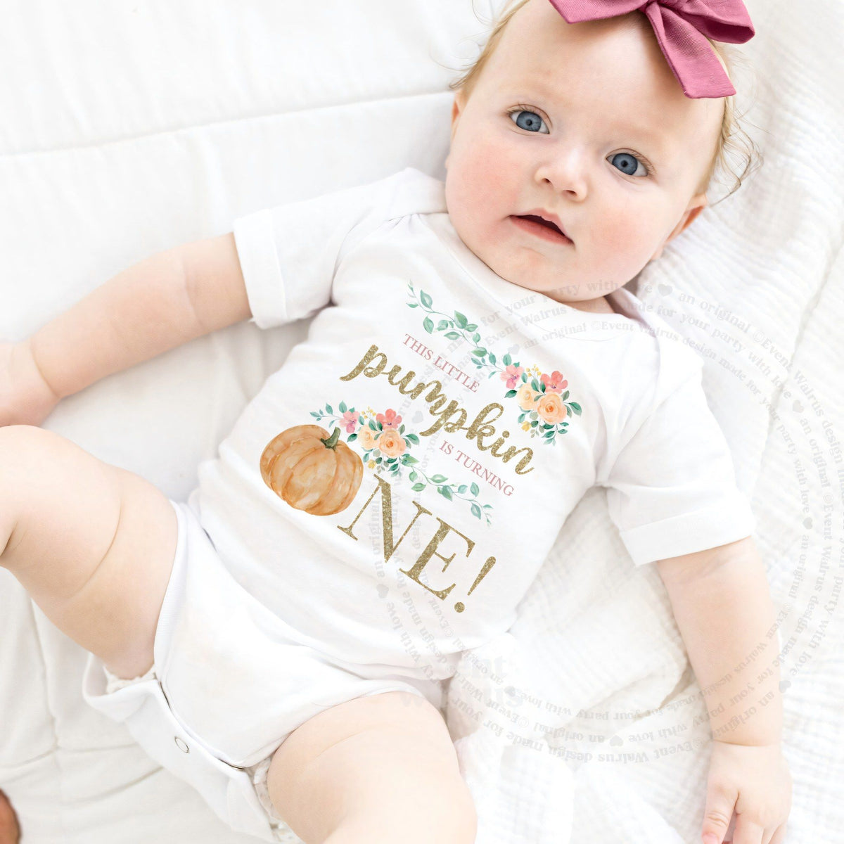 Baby girl with a pink bow lying in a white This Little Pumpkin Is Turning One bodysuit.