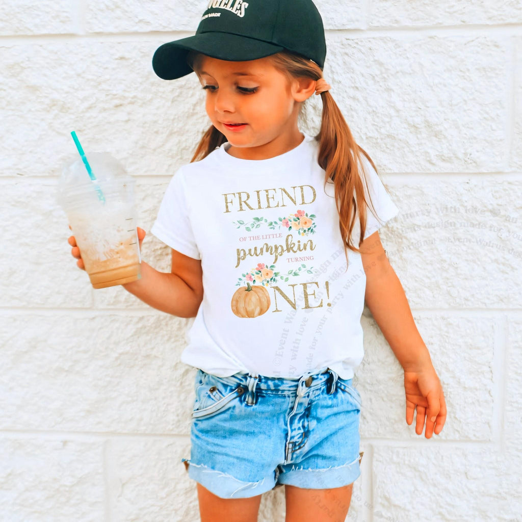 Girl in a ball cap holding a drink in a white Friend of the Little Pumpkin shirt.