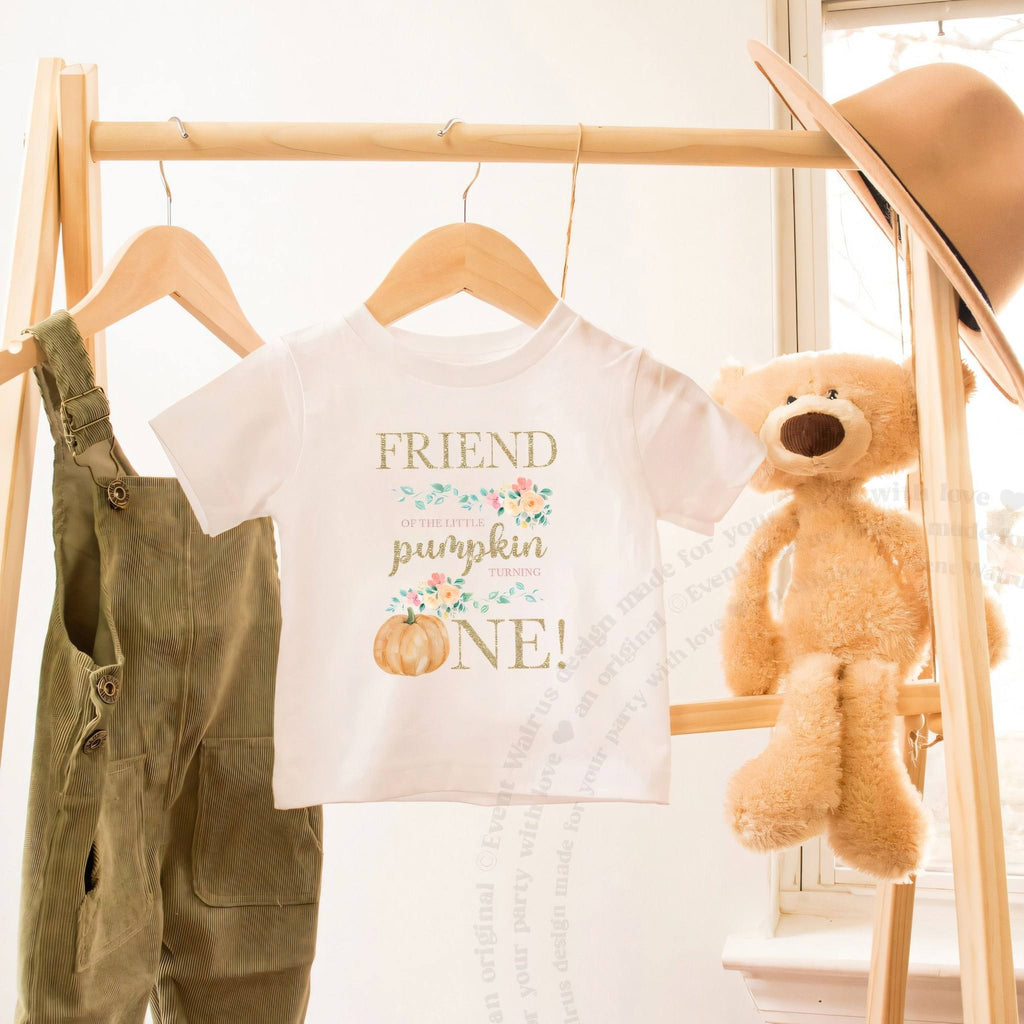 White Friend of the Little Pumpkin toddler tee on a wooden clothes rack beside a teddy bear.