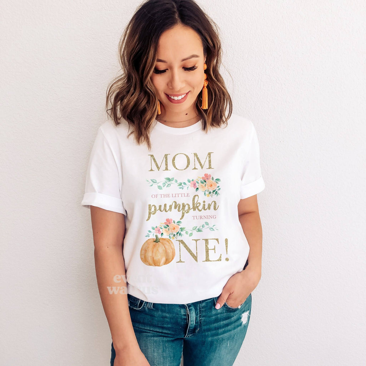Smiling woman in jeans wearing a white floral Mom of the Little Pumpkin shirt.