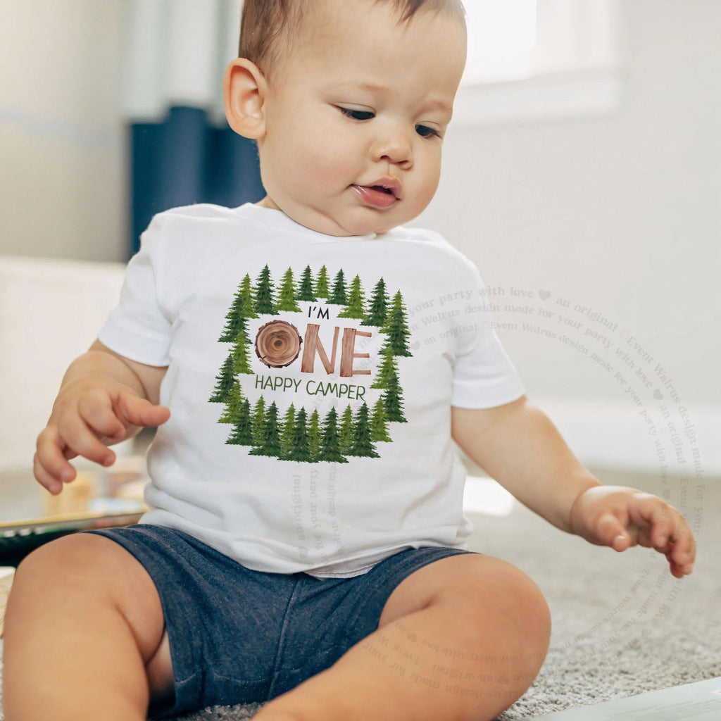 Baby boy sitting on a rug in a white I'm One Happy Camper baby tee.