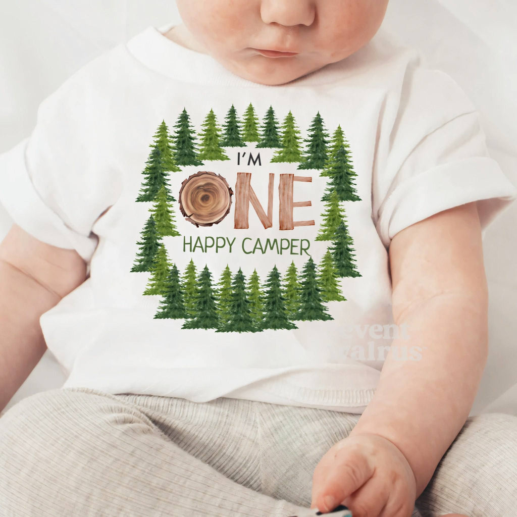 Baby sitting up in a white I'm One Happy Camper baby tee.