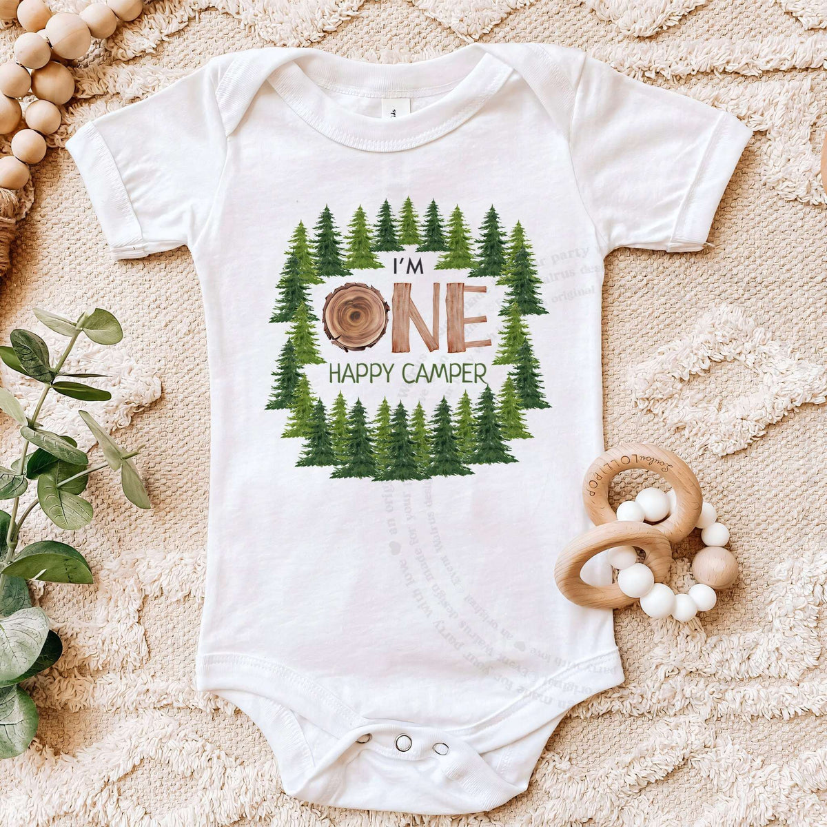 White I'm One Happy Camper bodysuit on a beige blanket with a wooden teether.