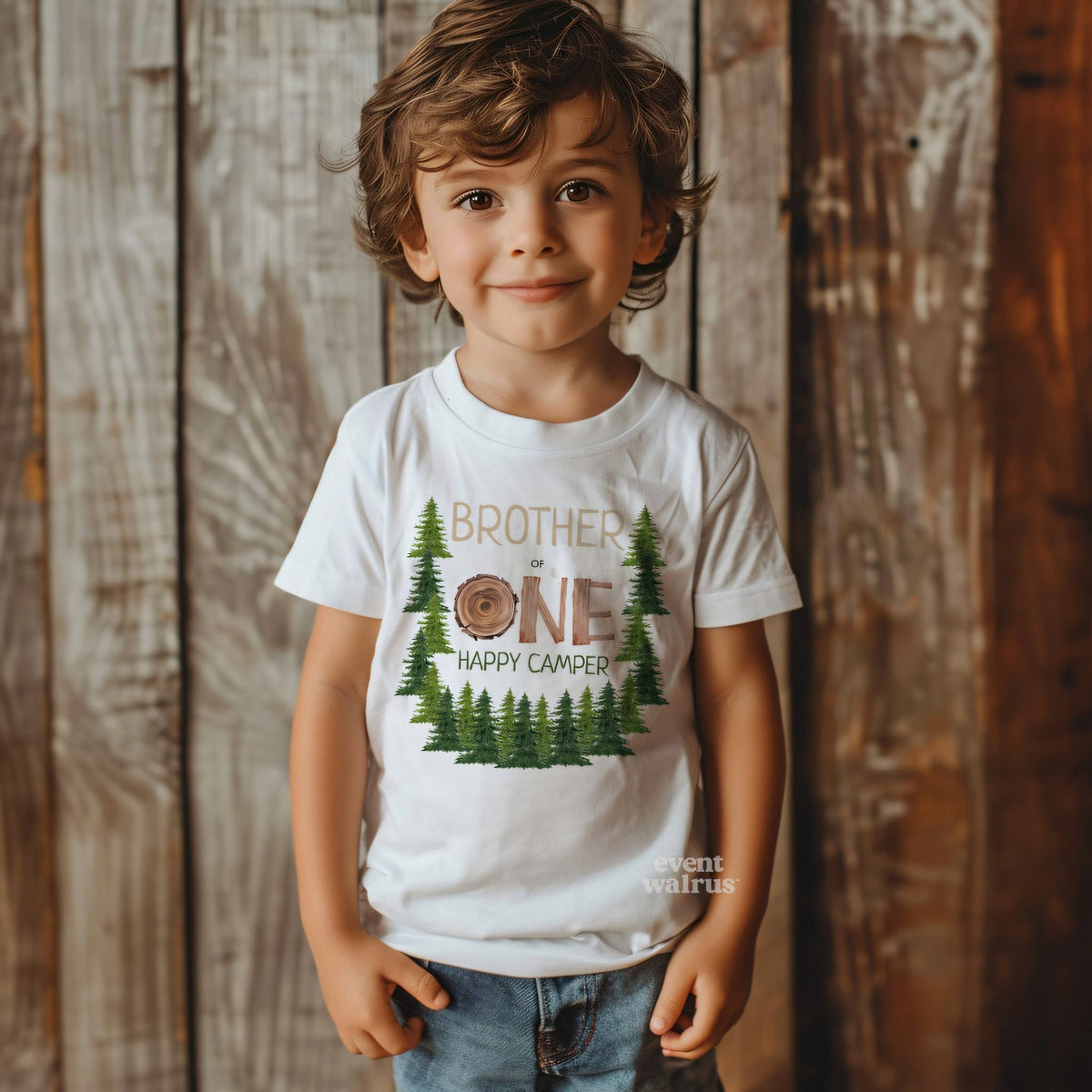 Little boy against a weathered wood wall in a white One Happy Camper tee.