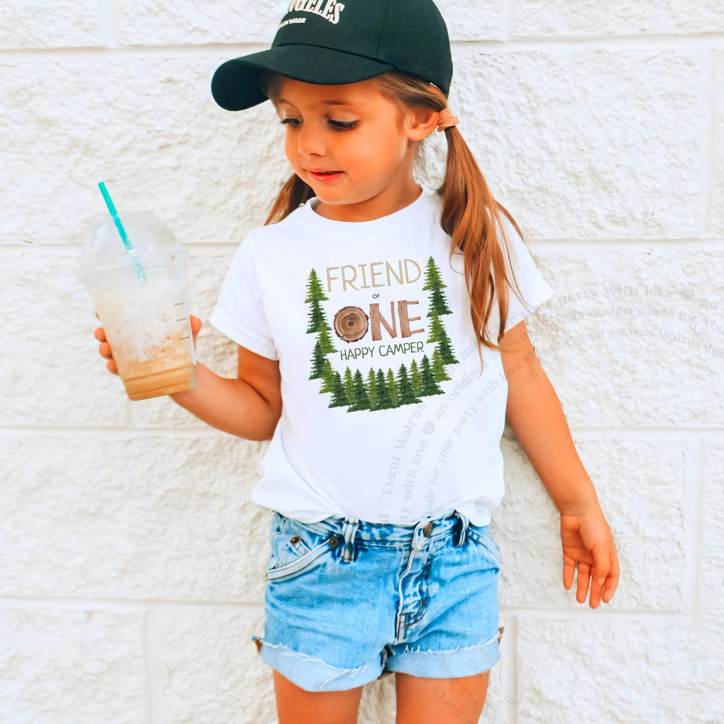 Girl in a ball cap holding a drink in a white Friend One Happy Camper shirt.
