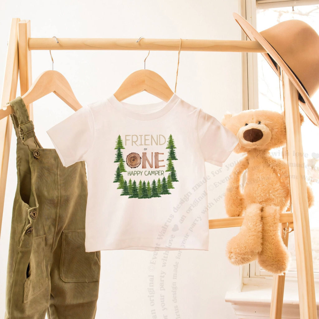 White Friend One Happy Camper toddler tee on a wooden clothes rack beside a teddy bear.